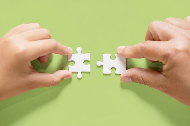 Hand connecting puzzle pieces table green